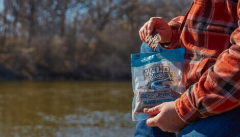 man eating peppered jerky out of the bag alongside a pond.